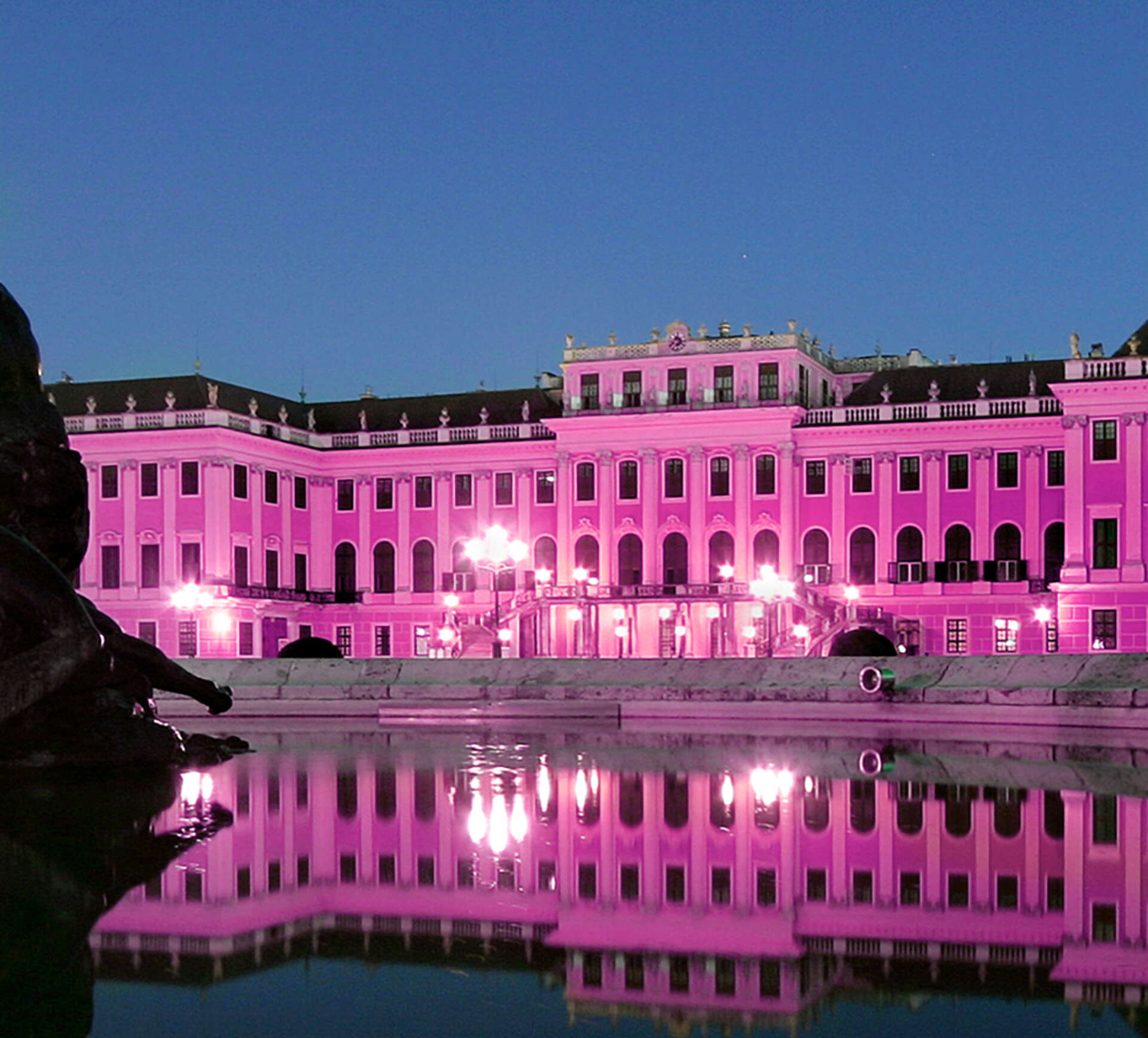 Schloss Schönbrunn pink beleuchtet, das Schloss spiegelt sich im Brunnen